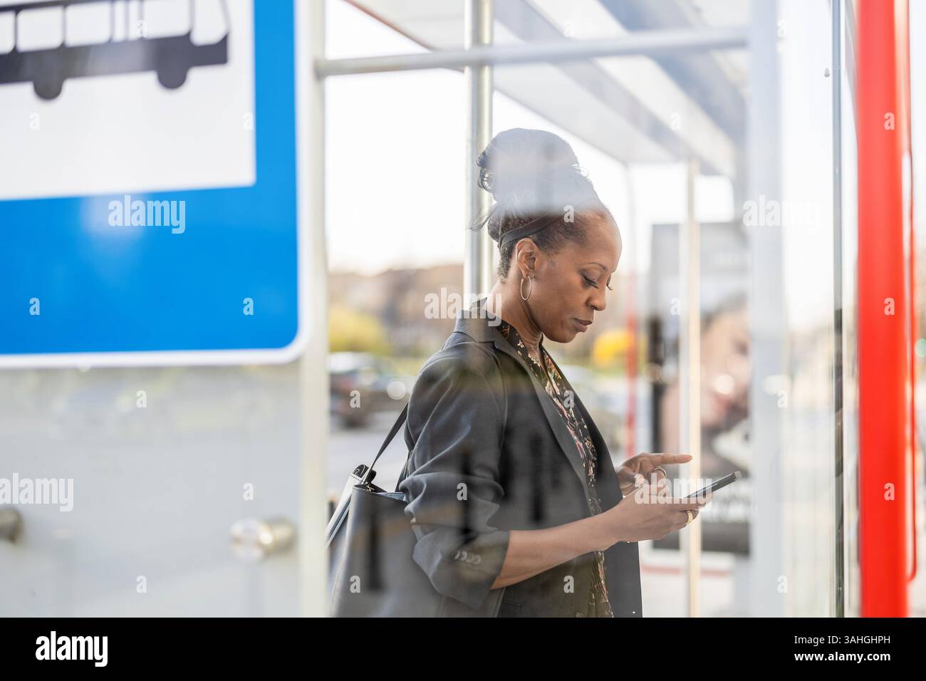 Donna che usa il suo cellulare a una fermata dell'autobus in città Foto Stock