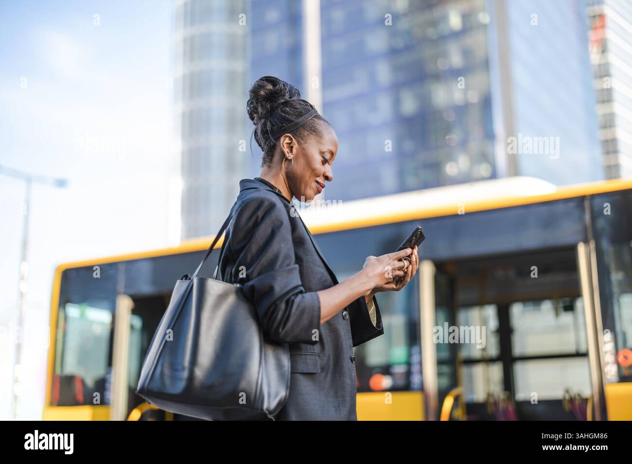 Donna che usa il suo cellulare a una fermata dell'autobus in città Foto Stock