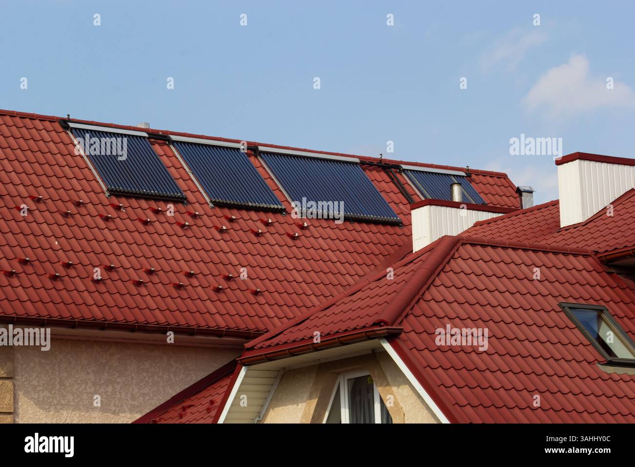 I pannelli solari sono montati su tetti di tegole rosse di case in un ambiente suburbano sotto cieli azzurri, mostrando l'integrazione di energie rinnovabili in Residen Foto Stock