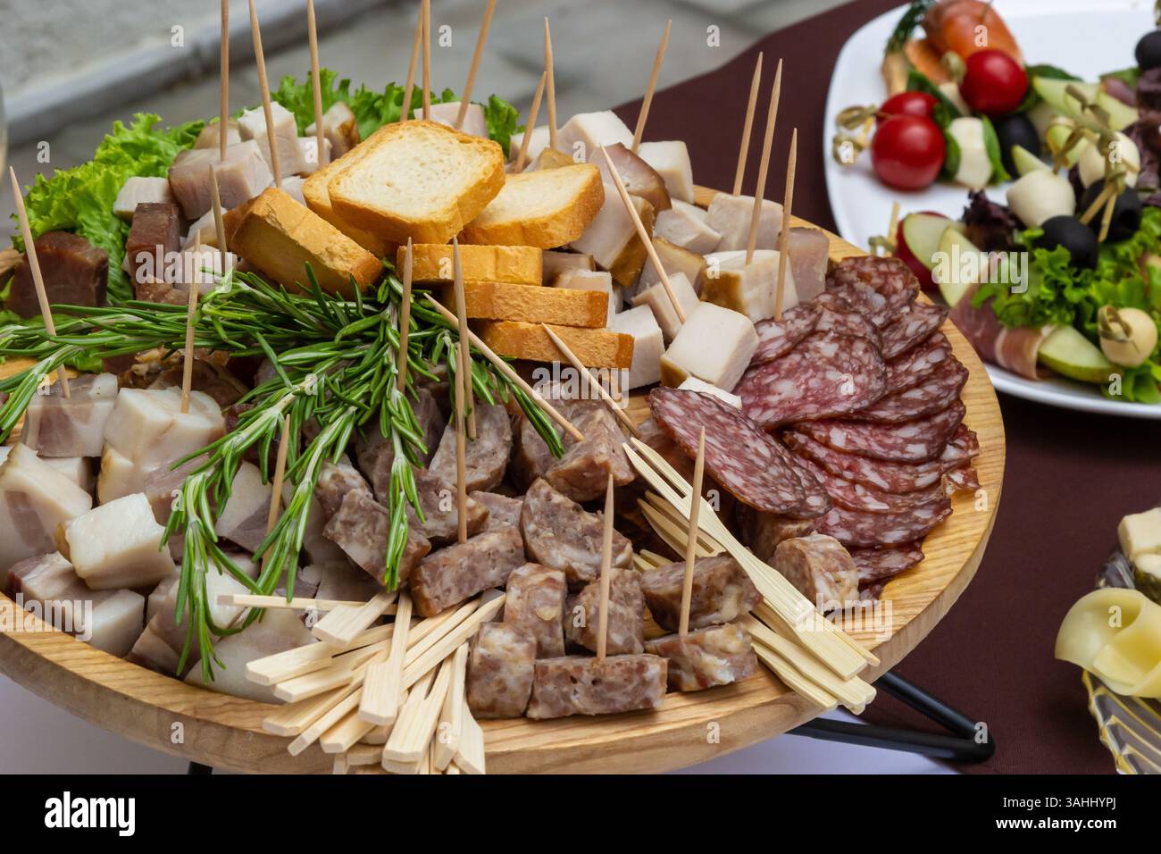 Un grande vassoio di legno mostra un assortimento di salumi, formaggi e pane, guarniti con erbe fresche. La diffusione fa parte di un evento culinario i Foto Stock
