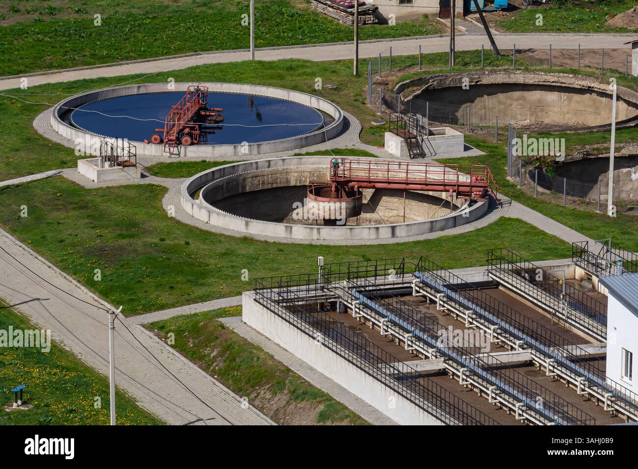 I serbatoi circolari e le attrezzature di trattamento per il trattamento delle acque reflue sono visibili in un'area verde. L'impianto mostra acqua limpida in un serbatoio e industria Foto Stock