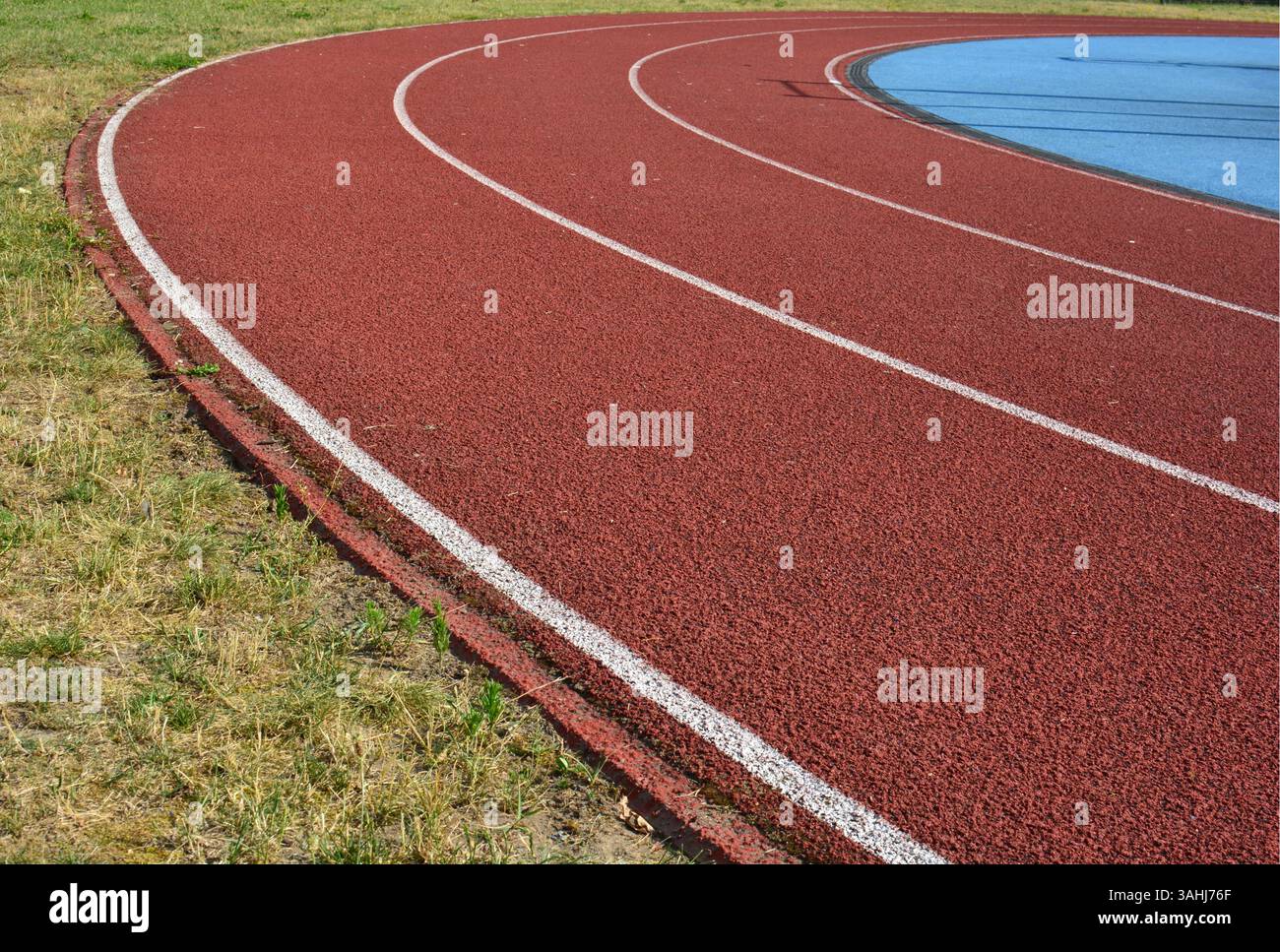 Pista da corsa rossa con erba sul lato sinistro e campo sportivo blu sul lato destro. Foto Stock