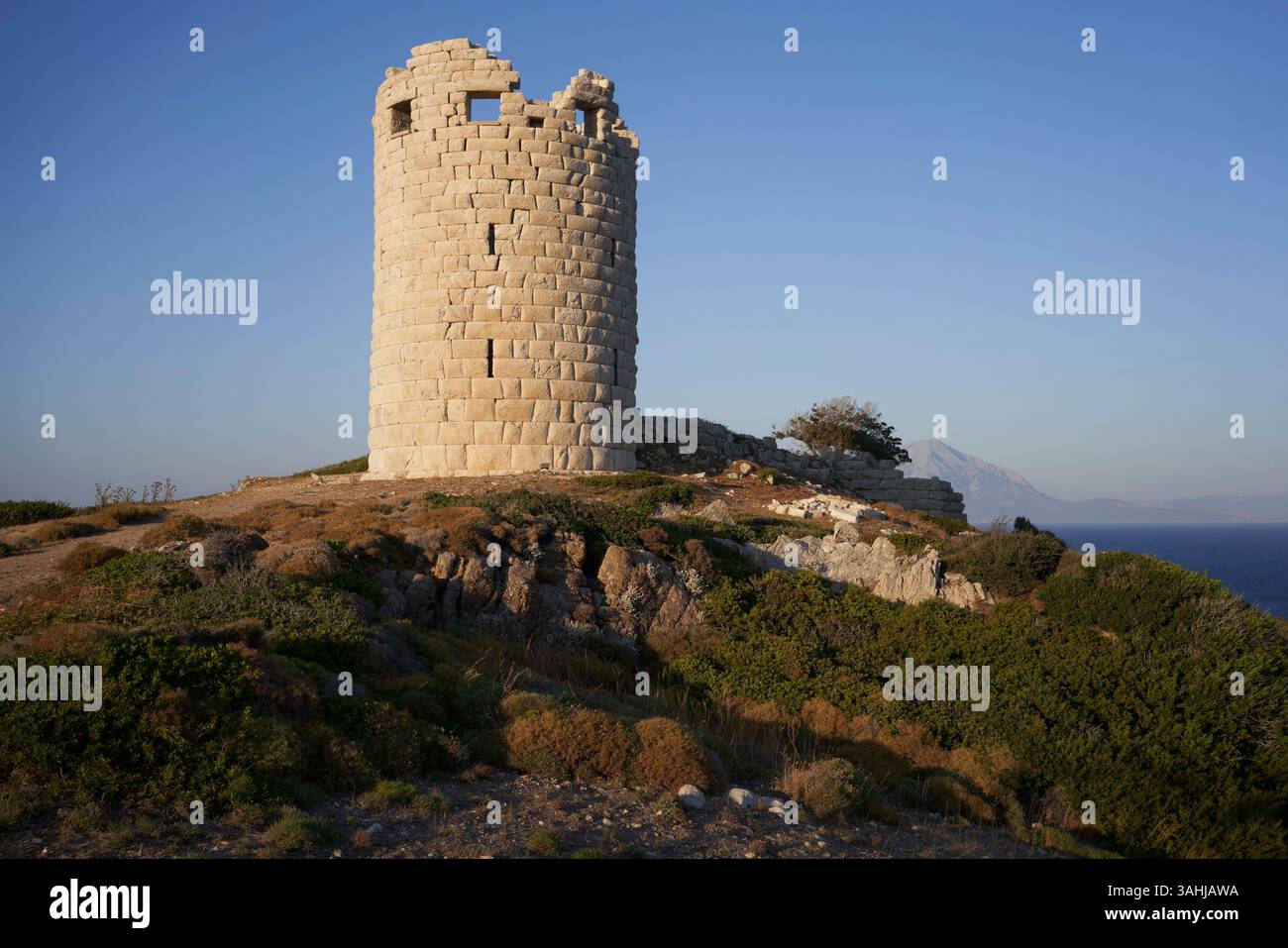 Antica torre in pietra su un'aspra collina con cielo azzurro e lontane viste sulle montagne. Foto Stock