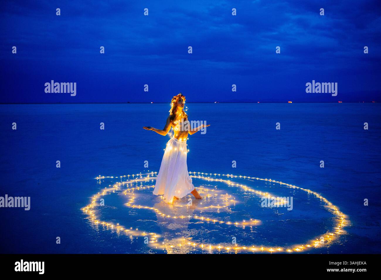 Una donna con un abito bianco è circondata da luci accese su una spiaggia blu serena al tramonto. Bonneville Salt Flats, Utah, Stati Uniti Foto Stock