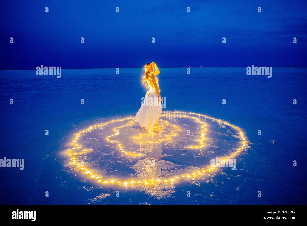 Una donna con un abito bianco si erge sull'acqua circondata da luci incandescenti sotto un cielo blu profondo. Bonneville Salt Flats, Utah, Stati Uniti Foto Stock