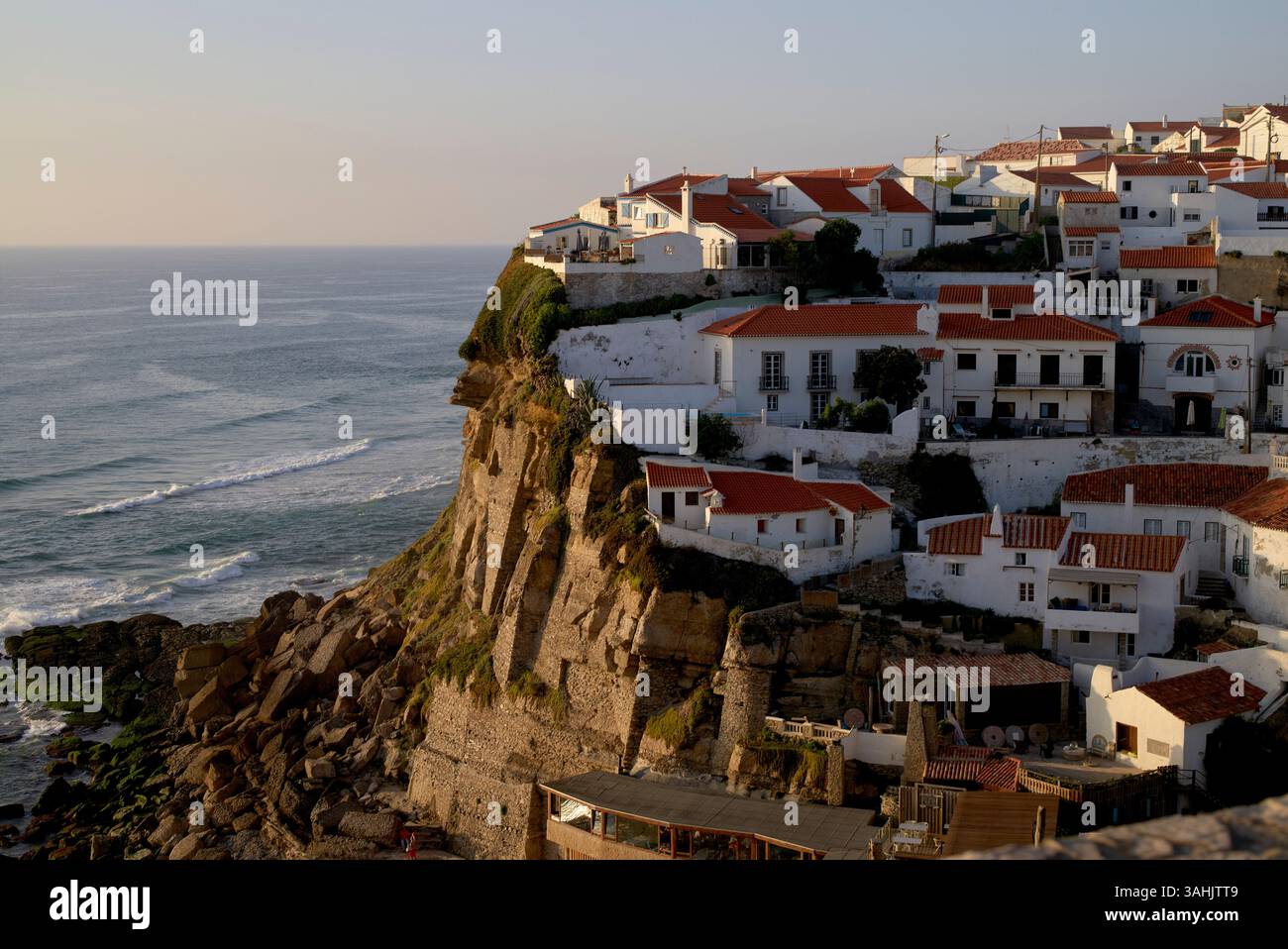Villaggio costiero sulla scogliera con case bianche e tetti rossi che si affacciano sull'oceano al tramonto. Foto Stock