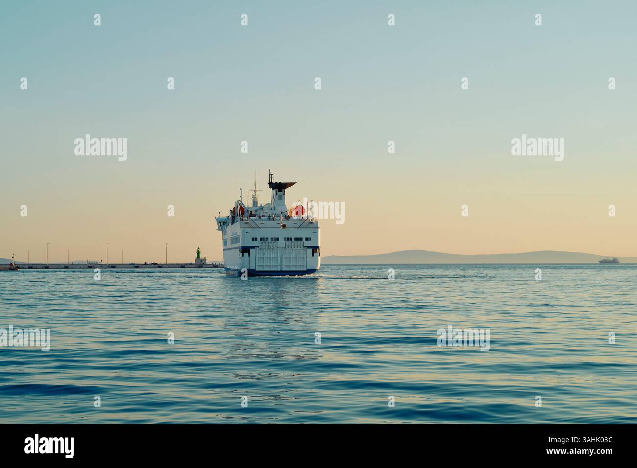 Grande traghetto che naviga sul mare calmo durante il cielo azzurro all'alba vicino a una costa lontana. Spalato, Croazia Foto Stock