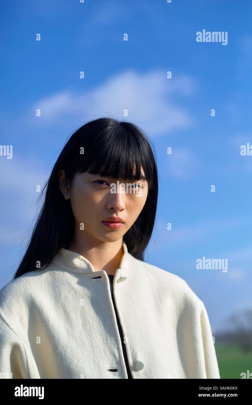 Donna con capelli neri e cappotto bianco su un cielo blu brillante con nuvole sparse. Brandeburgo, Germania Foto Stock