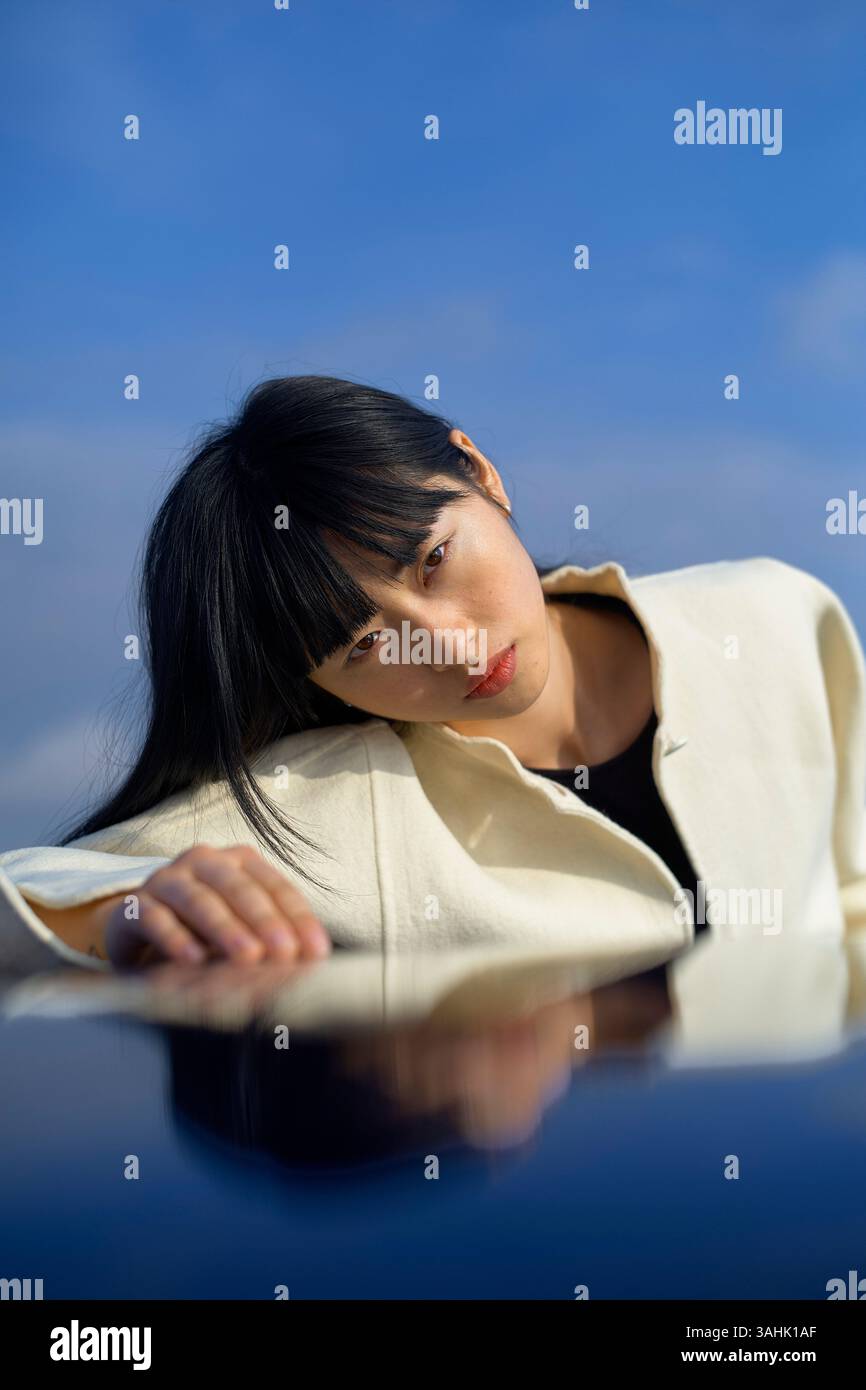 Donna con un cappotto bianco si appoggia su una superficie riflettente contro un cielo azzurro. Brandeburgo, Germania Foto Stock