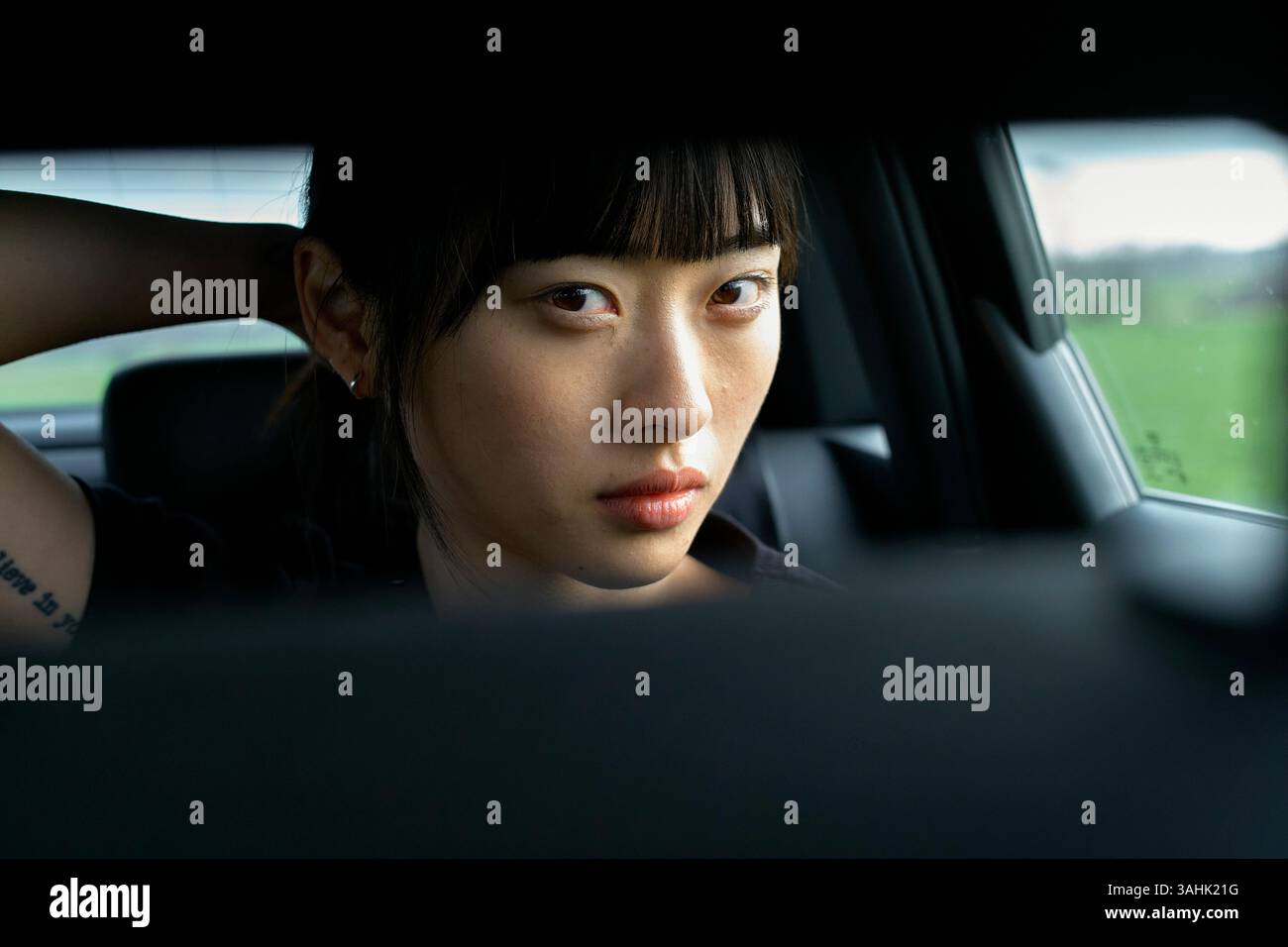Donna dall'espressione seria siede in auto, tenendo i capelli all'indietro, guardando la telecamera attraverso lo specchietto retrovisore. Brandeburgo, Germania Foto Stock