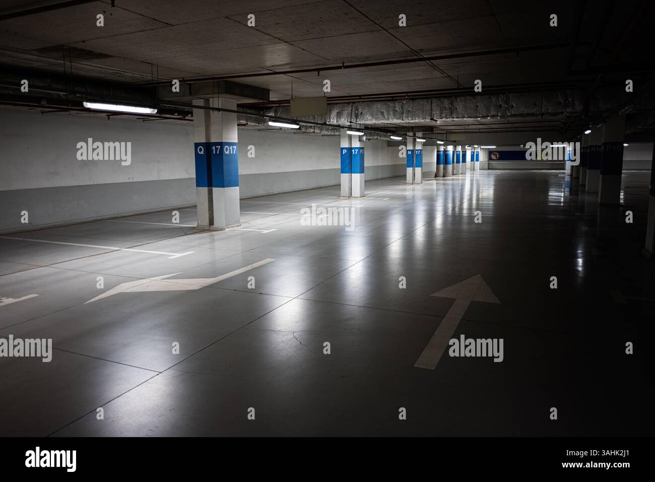 Ampio parcheggio sotterraneo con illuminazione riflettente e frecce direzionali Foto Stock