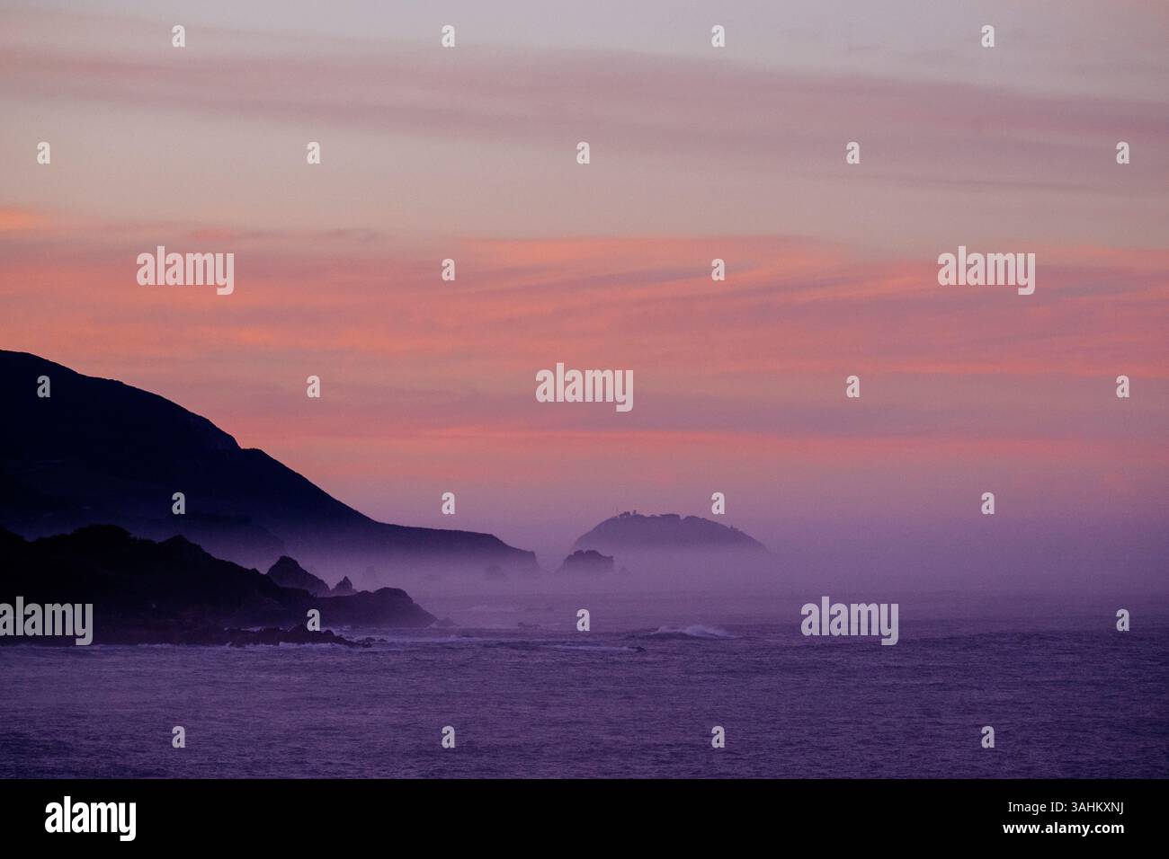 Serena vista dell'oceano al tramonto con montagne nebbiose all'orizzonte e cielo rosa-arancione. Monterey, CALIFORNIA, Stati Uniti Foto Stock