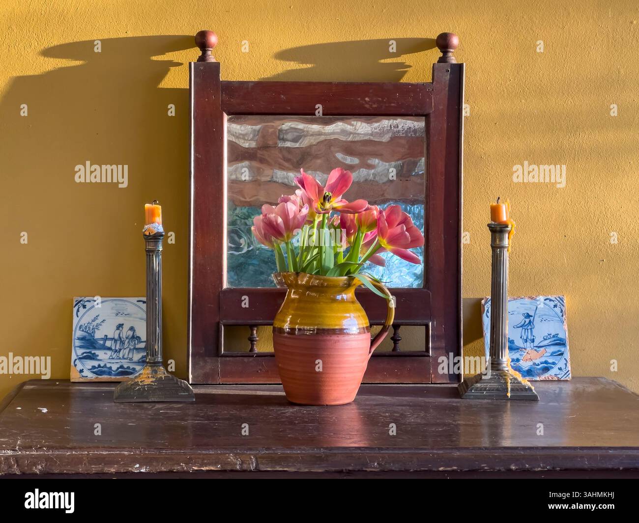 Una semplice disposizione a molla di tulipani in una vecchia brocca in terracotta, con candelabri d'argento e antiche piastrelle olandesi (Regno Unito) Foto Stock