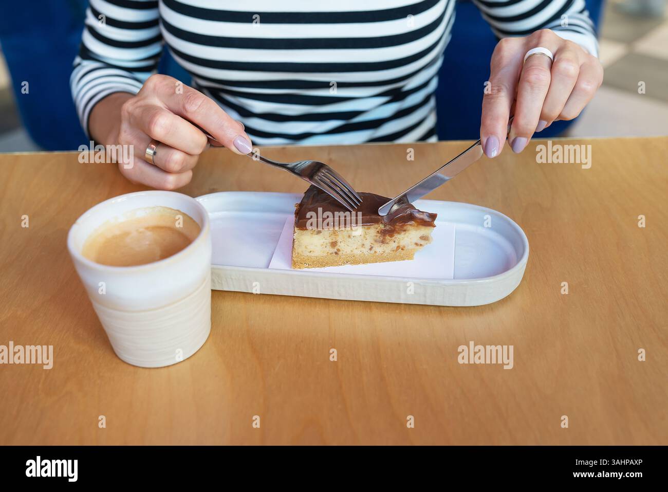 Una donna gode di una deliziosa fetta di torta al cioccolato con caffè in un caffè. Foto Stock