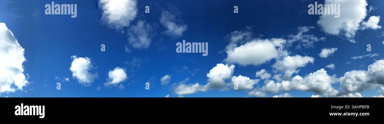 Una scena panoramica che mostra un cielo blu limpido pieno di nuvole bianche e soffici. Questo ambiente tranquillo e naturale evoca sensazioni di tranquillità e di relax Foto Stock