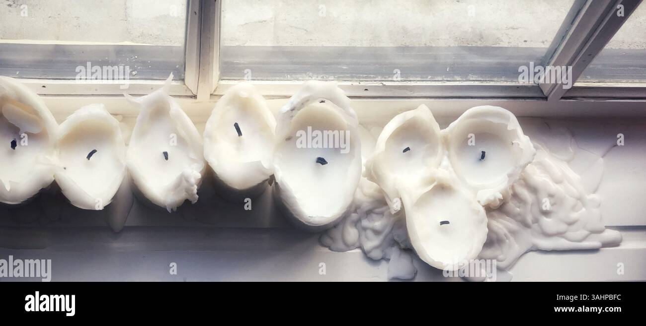 Un panorama dettagliato di candele bianche fuse posizionate vicino a una luminosa finestra. L'immagine mostra disegni artistici di cera ed esalta un sereno e un Foto Stock