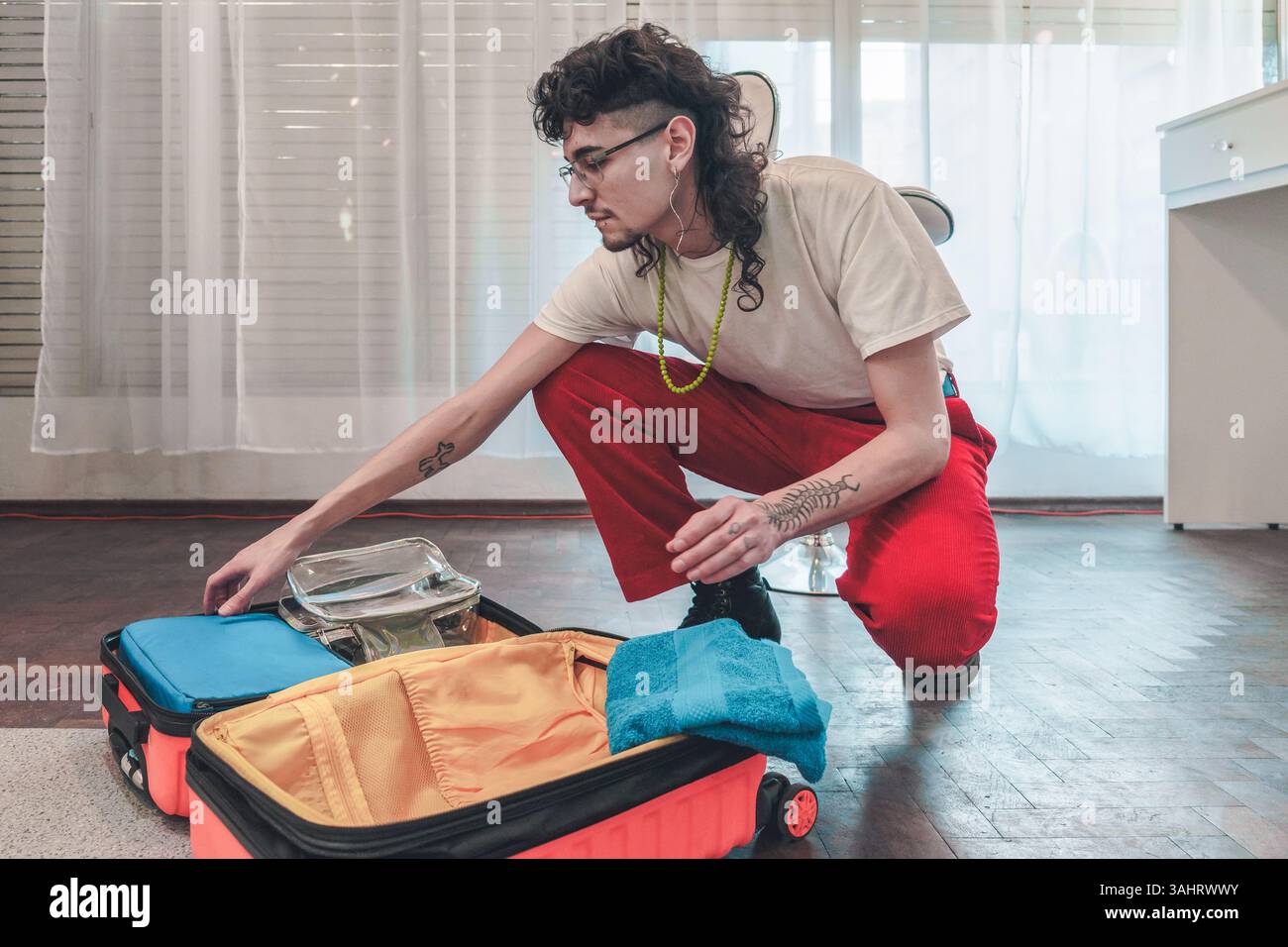 Giovane uomo elegante sta preparando con cura la valigia, organizzando abiti, accessori e articoli da toeletta, preparandosi per un viaggio o una vacanza entusiasmante Foto Stock