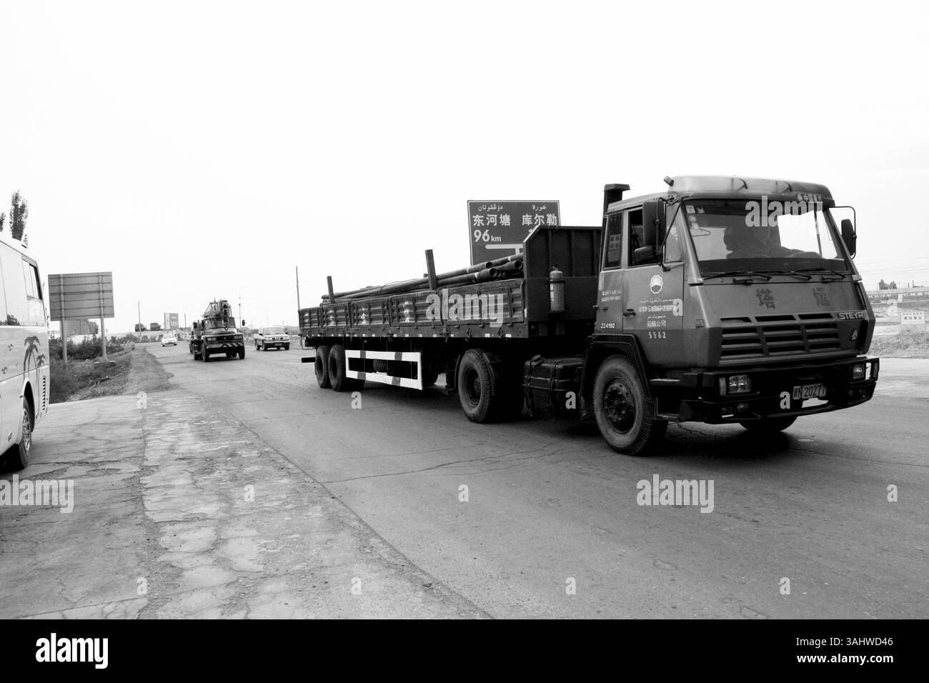 STEYR Truck navigando nel deserto meridionale dello Xinjiang per l'esplorazione petrolifera：questa fotografia in bianco e nero mostra un potente camion STEYR del comando di esplorazione del campo petrolifero di Tarim, navigando sulle vaste strade desertiche dello Xinjiang meridionale, in Cina. Il camion, carico di tubi per l'esplorazione petrolifera, è una parte essenziale del settore energetico, contribuendo a alimentare la crescente domanda cinese di petrolio. L'immagine evidenzia le condizioni difficili del deserto, con il camion che viaggia attraverso paesaggi remoti e aridi, mostrando l'infrastruttura robusta necessaria per l'esplorazione petrolifera in ambienti così estremi. Foto Stock