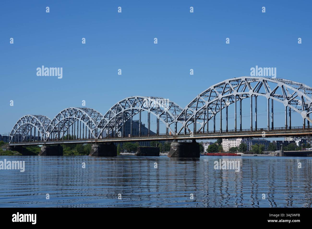 Una vista classica del Ponte della ferrovia di riga che attraversa il fiume Daugava, catturato dall'acqua in una giornata luminosa e soleggiata. Foto Stock