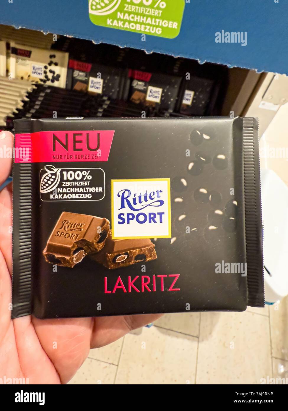 Primo piano di una nuova barretta di cioccolato ritter sport lakritz tenuta da una mano in un supermercato, che mette in evidenza il suo sapore unico e l'approvvigionamento sostenibile di cacao - Foto Stock