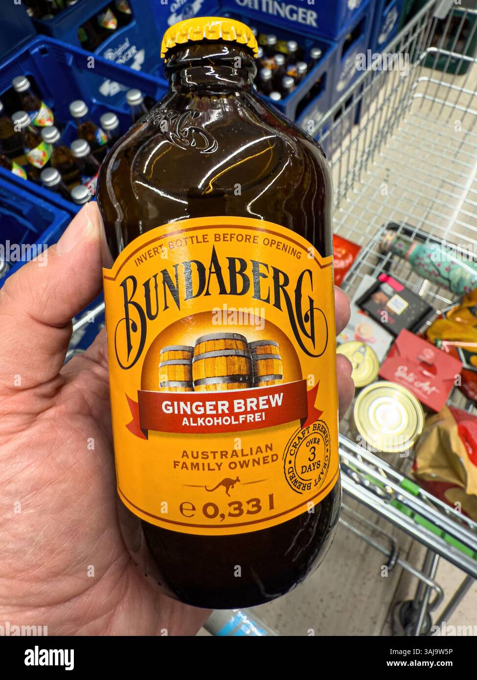 Primo piano di una mano che tiene una bottiglia di birra allo zenzero bundaberg in un supermercato, con altri prodotti sullo sfondo - FRANCOFORTE, GERMANIA - 9 APRILE 2025 Foto Stock