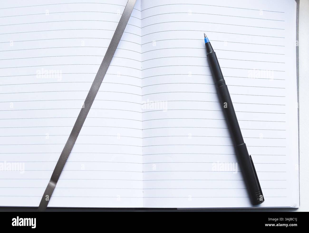 Una penna nera su un blocco appunti aperto con pagine rivestite e un segnaposto grigio a nastro Foto Stock