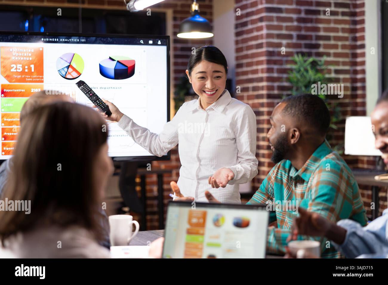Un'imprenditrice sorridente si impegna in un incontro notturno con i colleghi in un ufficio a muro. Allegro team di startup multietnico che collabora alla strategia di marketing e alle idee di brainstorming. Foto Stock
