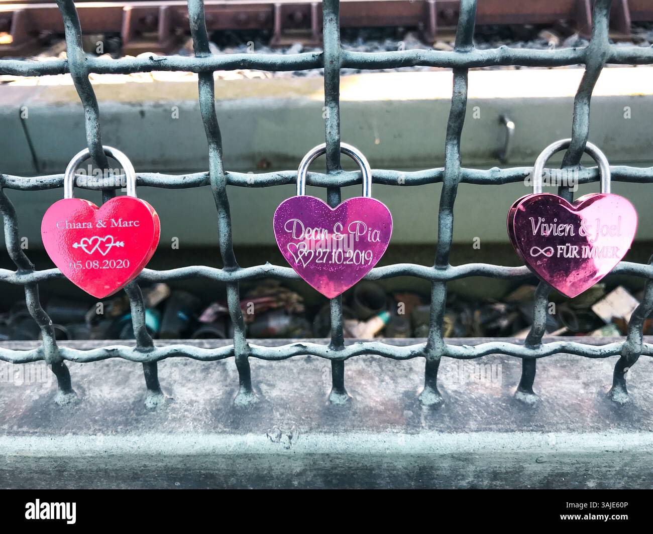 Colonia, Germania - 18 marzo 2022 tre chiuse a forma di cuore sono appese su una recinzione. Le serrature sono rosa e hanno i nomi della coppia che si è sposata Foto Stock
