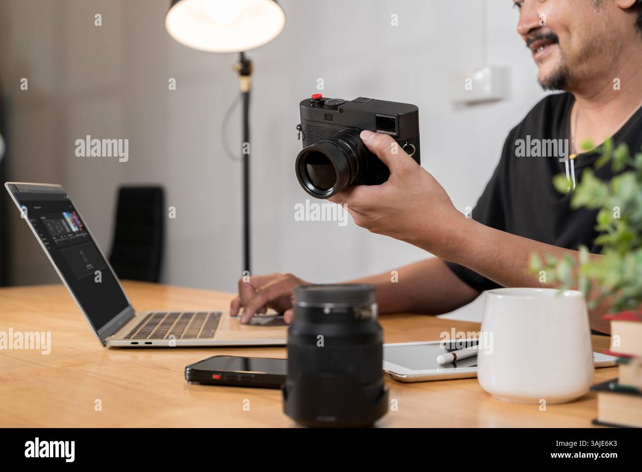 Giovane fotografo professionista impegnato nell'editing di foto su un computer portatile dallo studio domestico. Giovane fotografo con barba che modifica le foto a casa. Viaggio fotografico Foto Stock