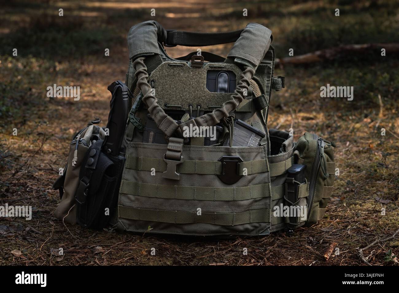 Gilet tattico Olive con smartphone per navigazione, coltello tattico e tasche nella foresta. Foto Stock