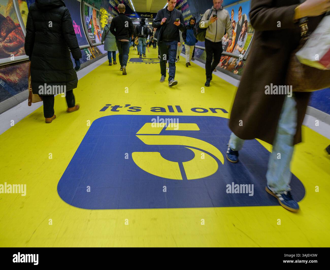 Il branding pubblicitario "IT's All on 5" è stato esposto in modo prominente in una vivace stazione della metropolitana di Londra, promuovendo Channel 5, un canale televisivo pubblico di trasmissione gratuita britannico di proprietà di Channel 5 Broadcasting Limited, parte della divisione UK and Australia di Paramount Global. Foto Stock