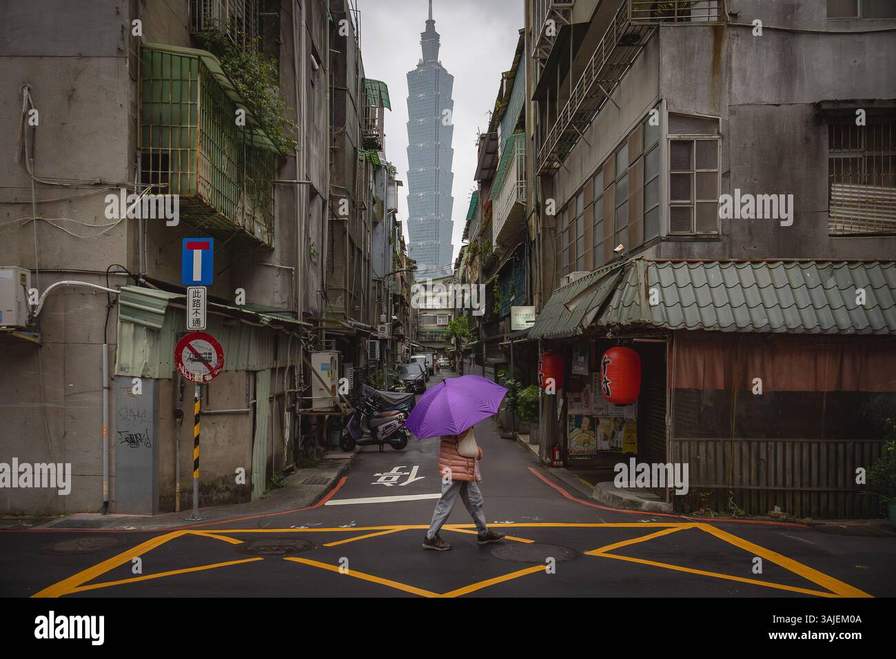 Persona con in mano un ombrello viola e un edificio Taipei 101 sullo sfondo di una strada cittadina a Taiwan. Foto scattata su una nuvolosa in una giornata nuvolosa Foto Stock