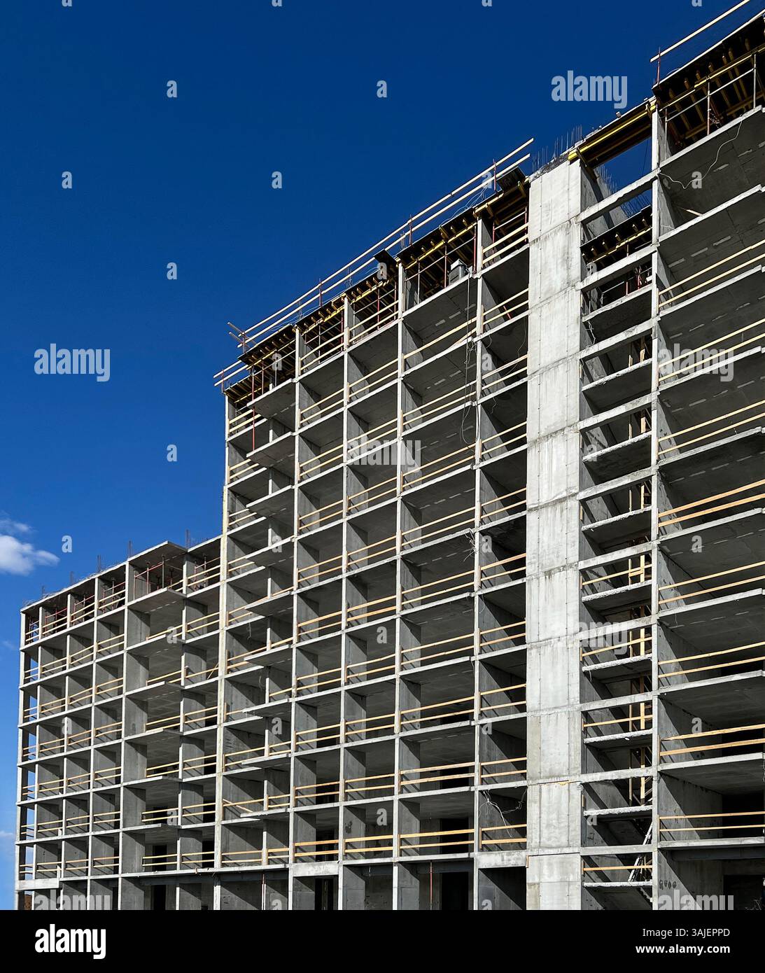 Alto edificio in costruzione con struttura in cemento a vista e ponteggi in legno sotto un chiaro sfondo blu del cielo, moderno sviluppo urbano Foto Stock