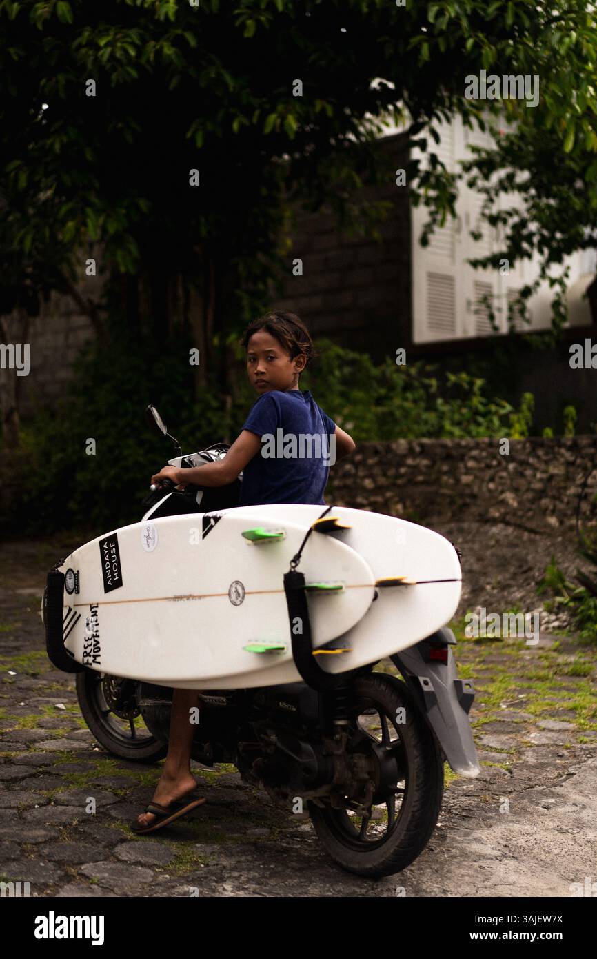 Un ragazzo indonesiano va in bicicletta per fare surf Foto Stock