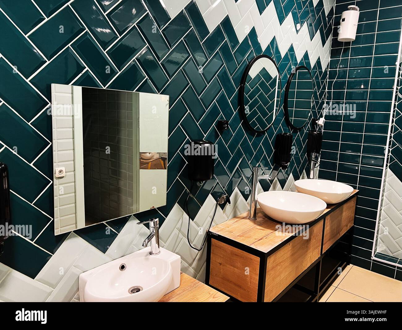 Un bagno contemporaneo con piastrelle eleganti, specchi rotondi e doppi lavandini. Foto Stock