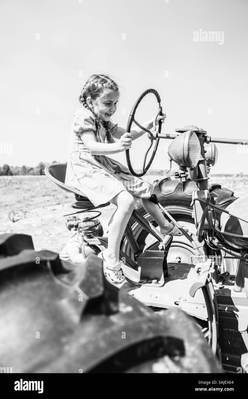 Una ragazza sorridente guida un trattore d'epoca con un'immagine in bianco e nero Foto Stock