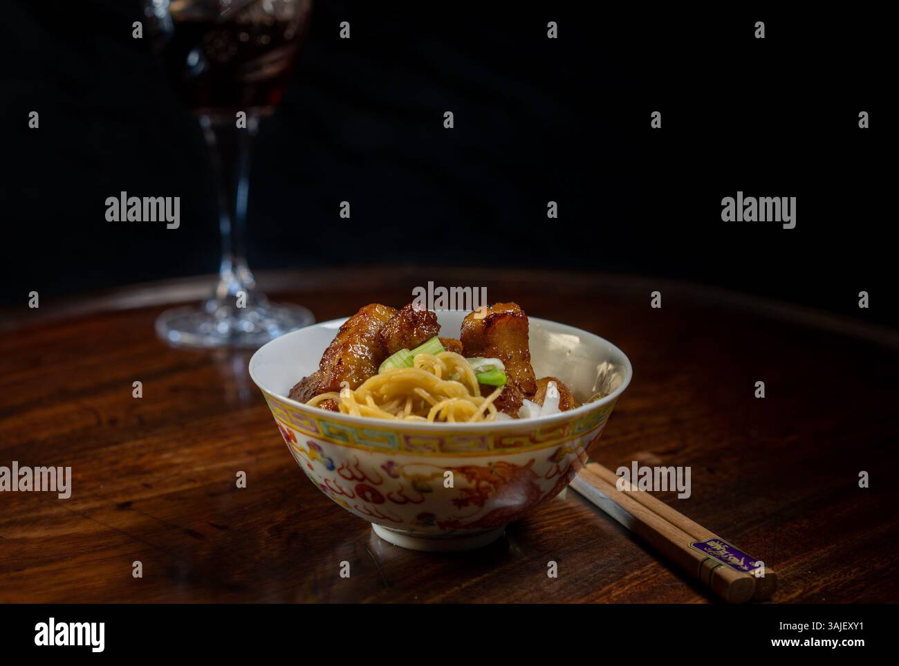 Piccola ciotola di spaghetti e pollo con bacchette sul tavolo e bicchiere sullo sfondo Foto Stock