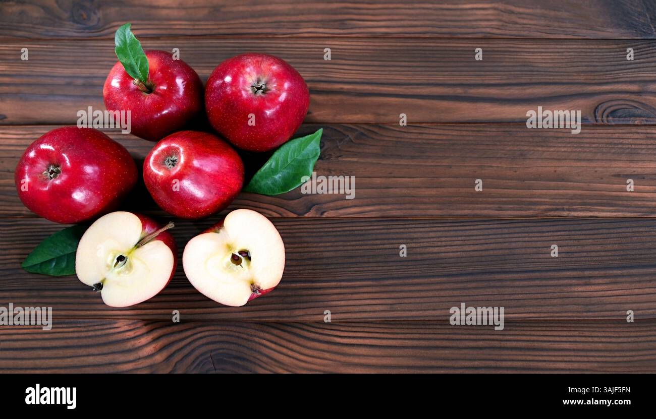 Mele rosse fresche su superficie in legno. Un primo piano di cinque mele rosse disposte su una superficie di legno, con due mele tagliate a metà per rivelare il loro succoso Foto Stock