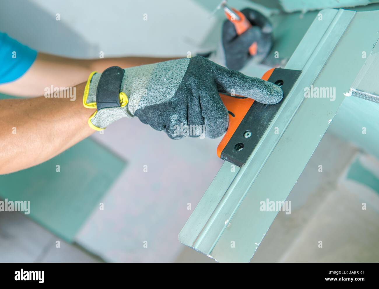 Una persona che indossa guanti protettivi sta applicando uno strumento di levigatura su una superficie di un'officina. L'attenzione è concentrata sull'attenta manipolazione dello strumento, ensu Foto Stock