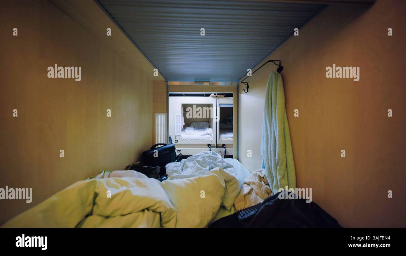 Camera d'albergo con capsula disordinata con letto e asciugamano appesi Foto Stock