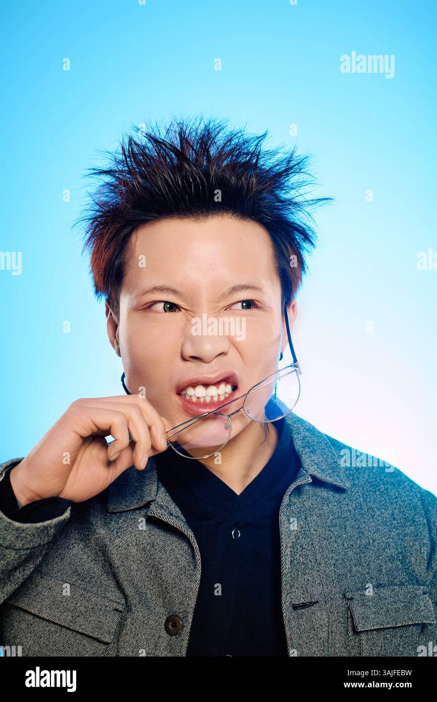Un bel giovane con i capelli piccanti si impegna in un momento giocoso, mordendo gli occhiali mentre posa. Foto Stock
