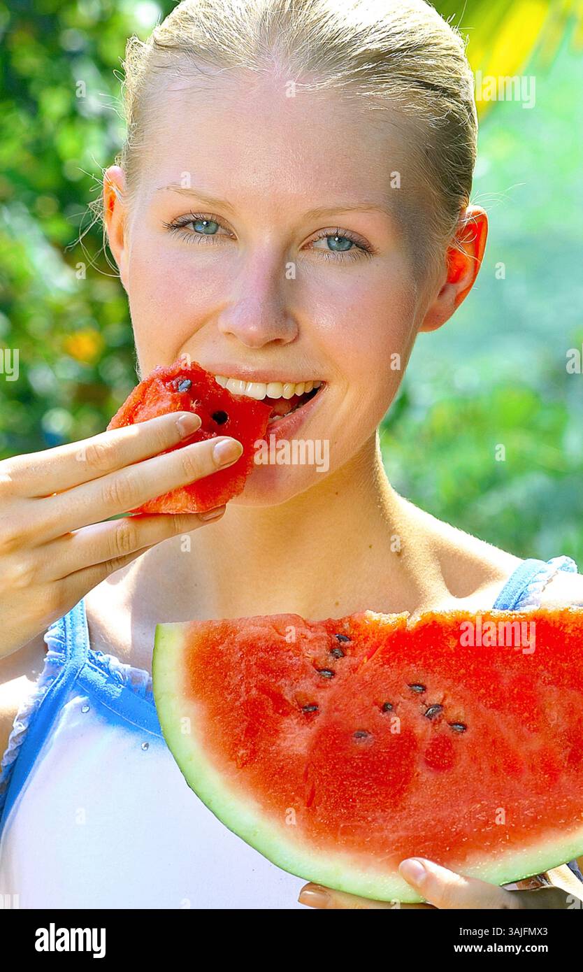 Primo piano di una giovane donna sorridente che mangia un pezzo di anguria con la mano, ritratto Foto Stock