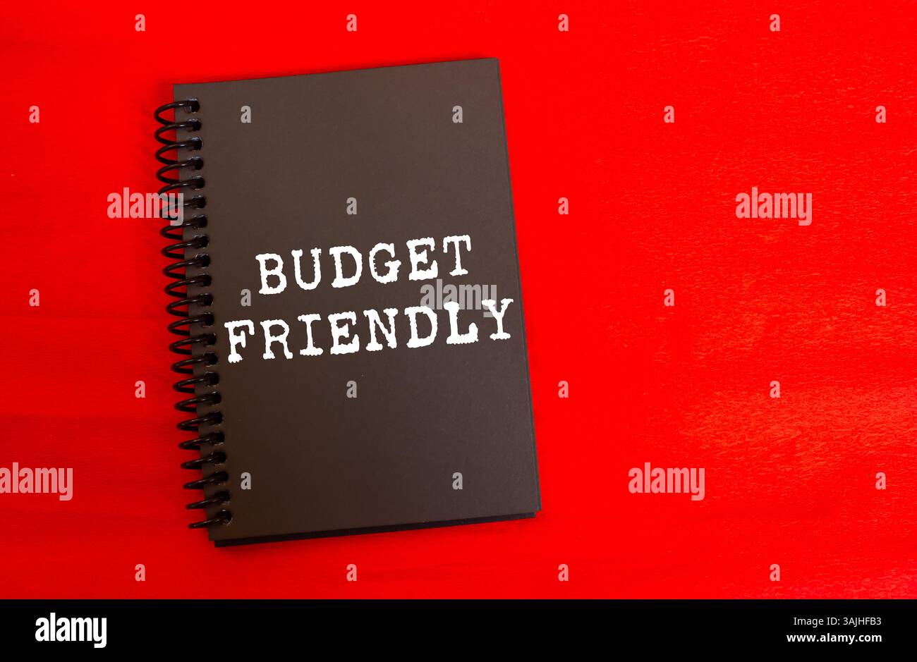 Messaggio economico scritto su una pagina nera del notebook su sfondo rosso. Simbolo di budget concettuale. Copia spazio. Foto Stock