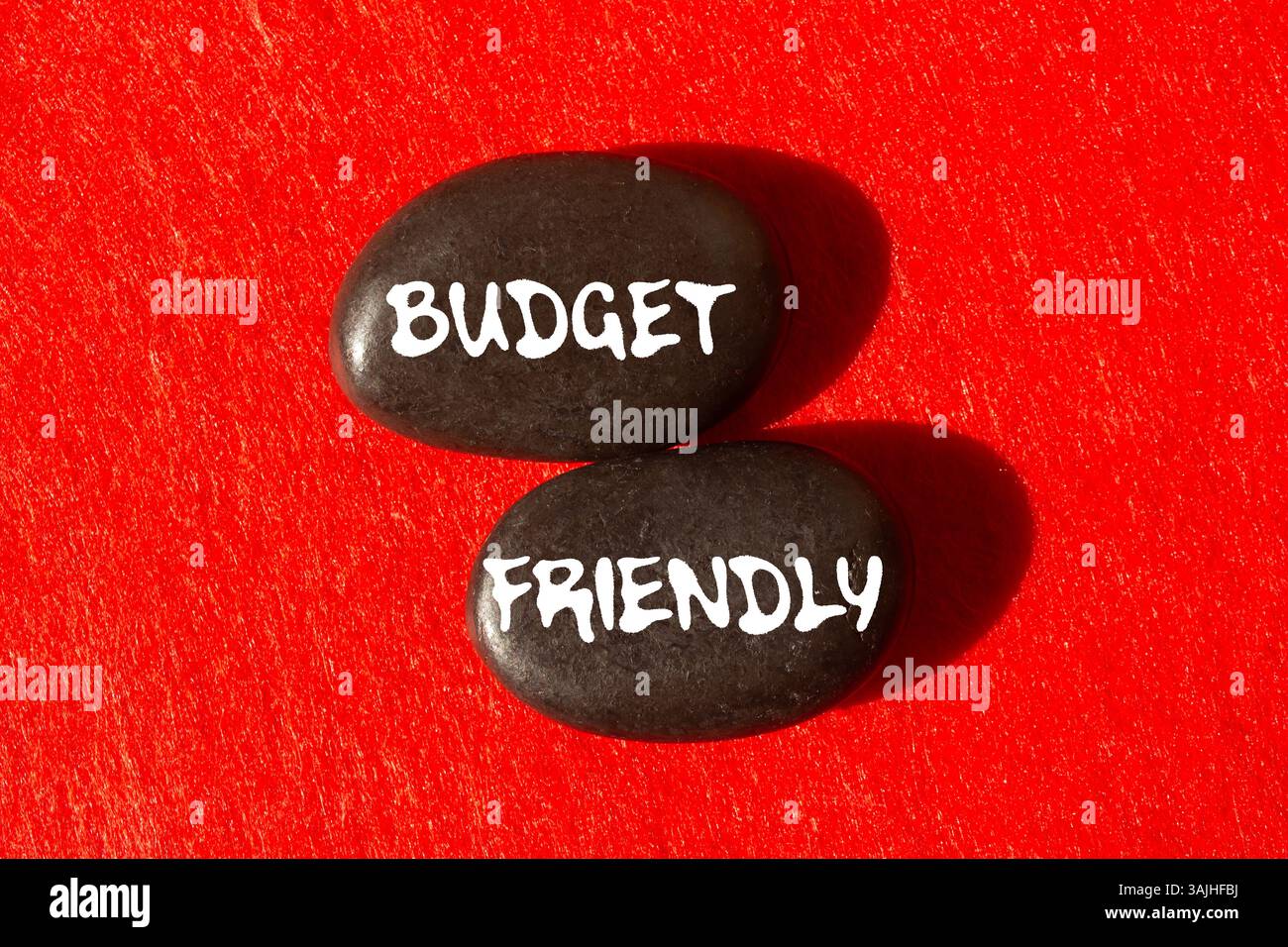 Messaggio economico scritto su pietre nere su sfondo rosso. Simbolo di budget concettuale. Copia spazio. Foto Stock