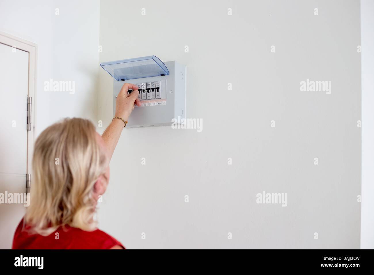 Uomo che regola gli interruttori automatici su pannello elettrico montati su una parete bianca in appartamento, spazio di copia. Foto Stock
