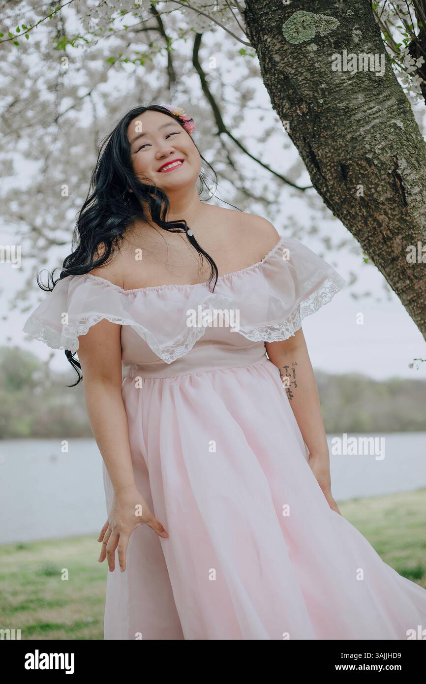 Donna asiatica con capelli lunghi che indossa un abito lungo rosa sullo sfondo di fiori di ciliegio a Philadelphia, Pennsylvania, USA Foto Stock