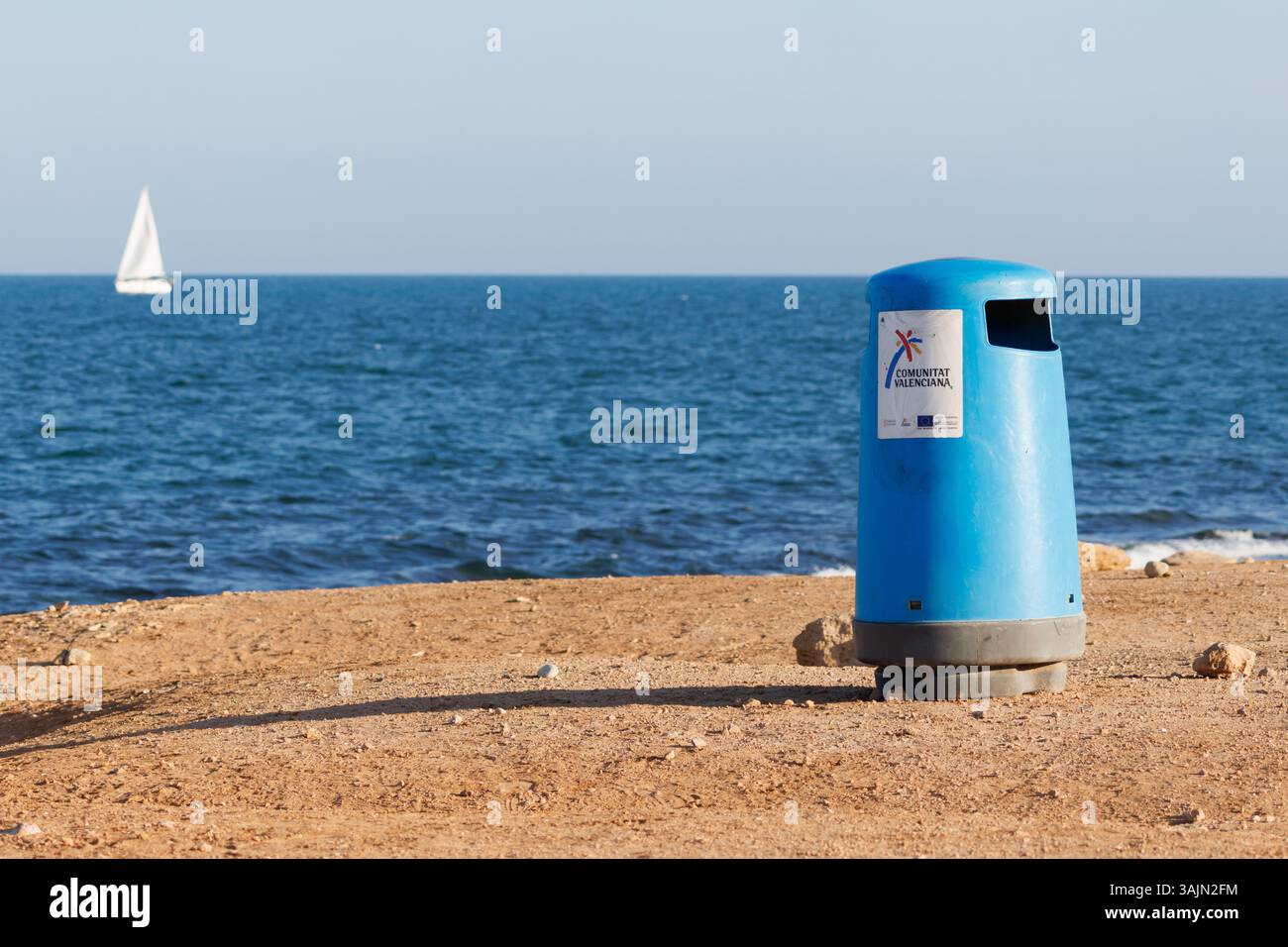 Cestino sulla spiaggia della Comunità Valenciana con il Mar Mediterraneo sullo sfondo e una barca a vela fuori fuoco Foto Stock