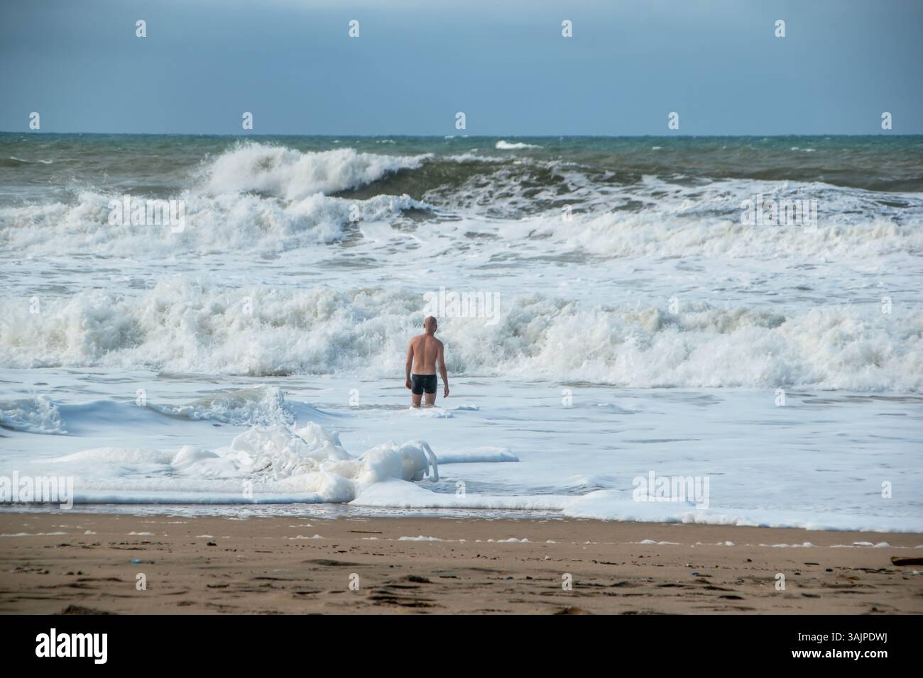 uomo avventuroso nell'oceano, di fronte a forti onde e condizioni pericolose su nuvole di tempesta vuote sulla spiaggia sullo sfondo Foto Stock
