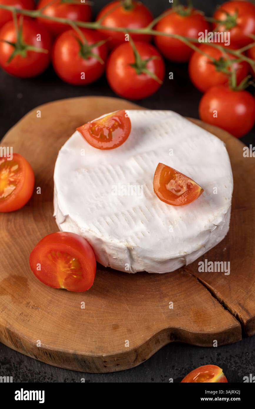un formaggio con muffa e pomodori rossi maturi, un pezzo di formaggio morbido maturo e alcuni piccoli pomodori rossi rotondi sul tavolo, primo piano Foto Stock