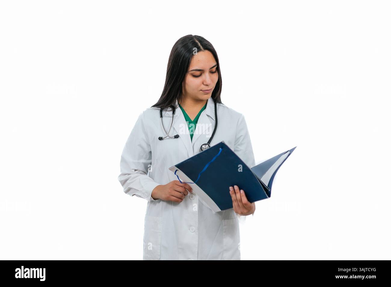 Una giovane donna che indossa un camice da laboratorio e uno stetoscopio sta leggendo attentamente le cartelle cliniche di un paziente su sfondo bianco, trasmettendo professionalità Foto Stock